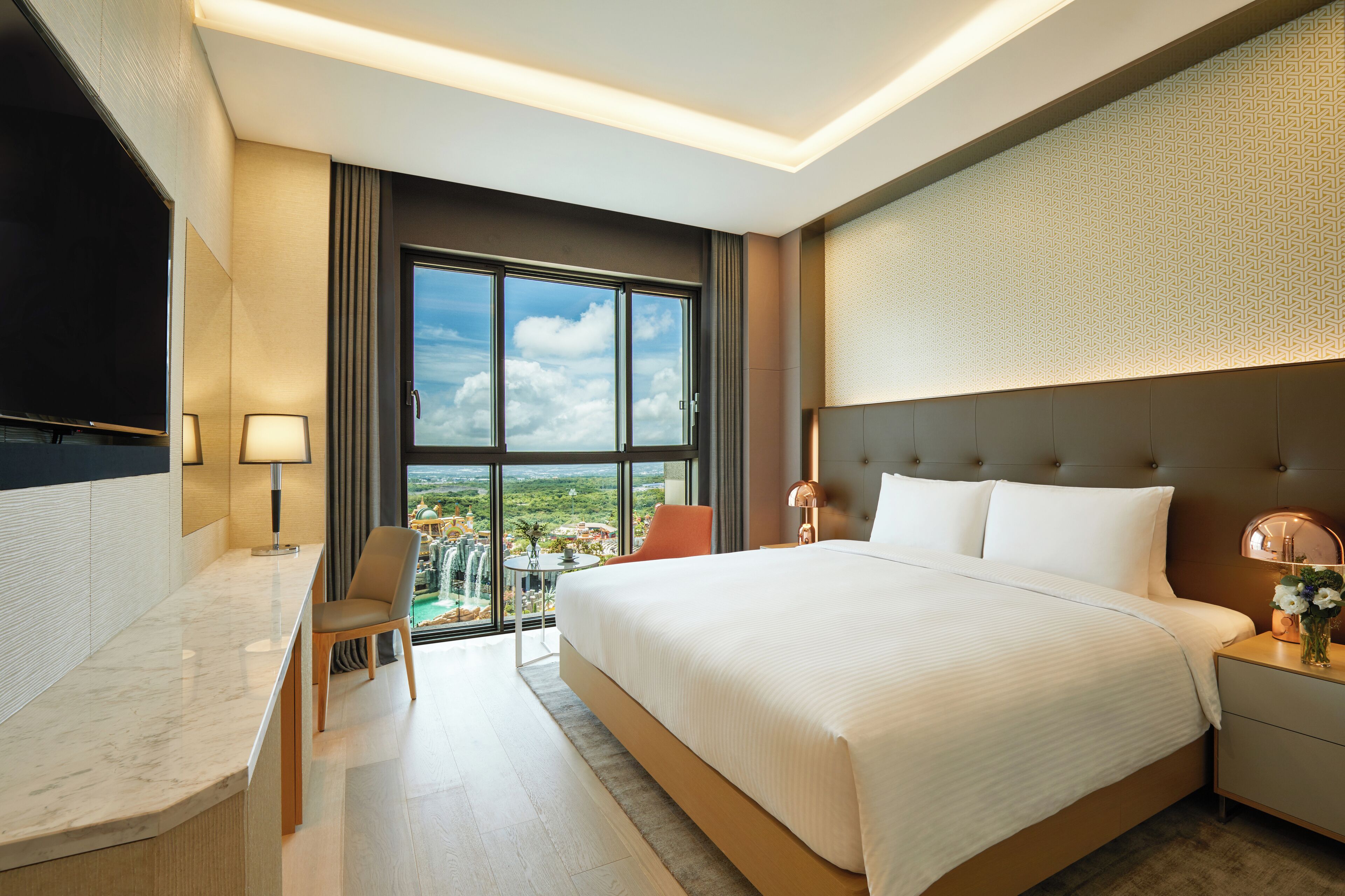 A modern hotel room with a large bed, a desk, a chair, and a television.