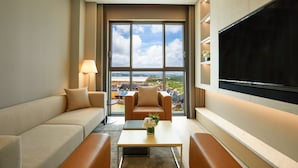 A modern hotel room with a large window offering a city view, a flat-screen TV mounted on the wall, and a comfortable seating area with a sofa and armchairs. - Shinhwa Jeju Shinhwa World Hotel & Resorts (Seogwipo)