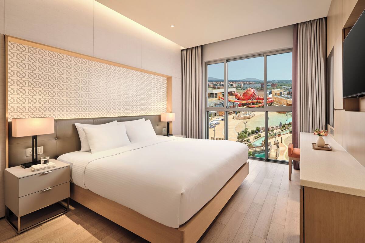 Une chambre d’hôtel moderne dotée d’un grand lit, d’une table de chevet, d’une télévision et offrant une vue sur un parc aquatique.