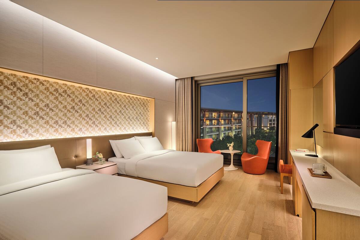 Une chambre d’hôtel moderne équipée de deux lits, d’un bureau, d’une chaise et d’une grande fenêtre donnant sur la ville.