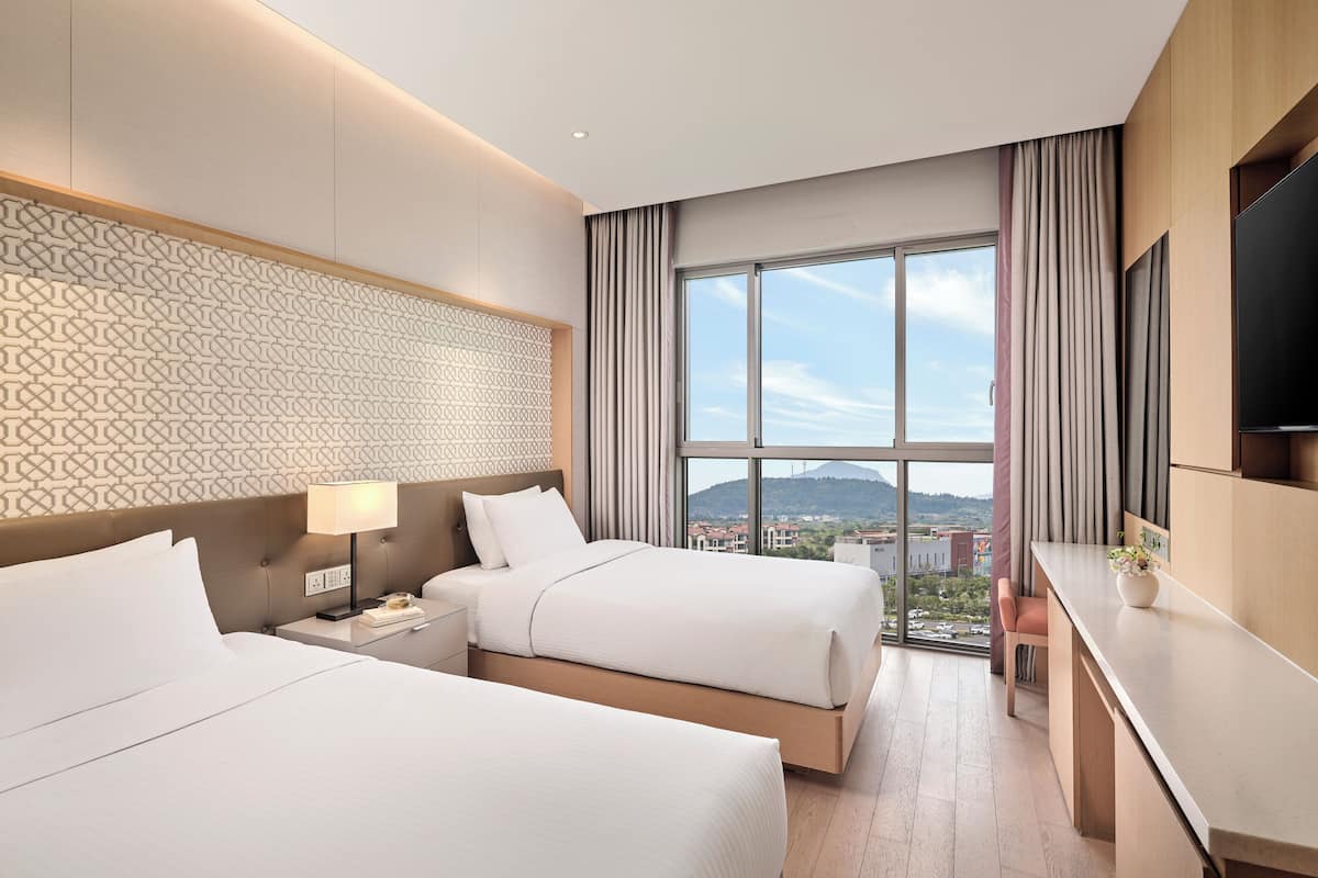 Une chambre d’hôtel avec deux lits, un bureau, une télévision et une grande fenêtre donnant sur la ville.