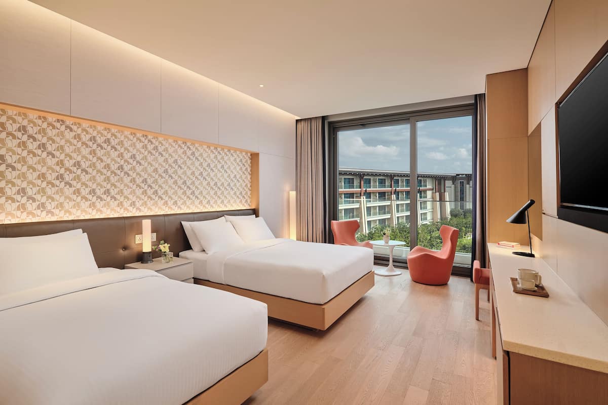Une chambre d’hôtel moderne, équipée de deux lits, d’un bureau, d’une chaise et d’une grande fenêtre donnant sur la ville.