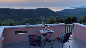 A terrace with a table set for two, overlooking a scenic landscape with hills and a body of water. - Apartment in private house with small terrace, panoramic view, external veranda (Magomadas)