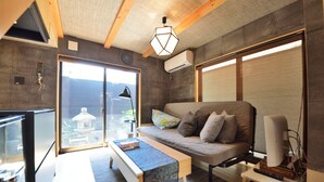 Una sala de estar moderna con un sofá, una mesa de centro y un televisor. Se aprecia una ventana grande con vistas a un edificio.