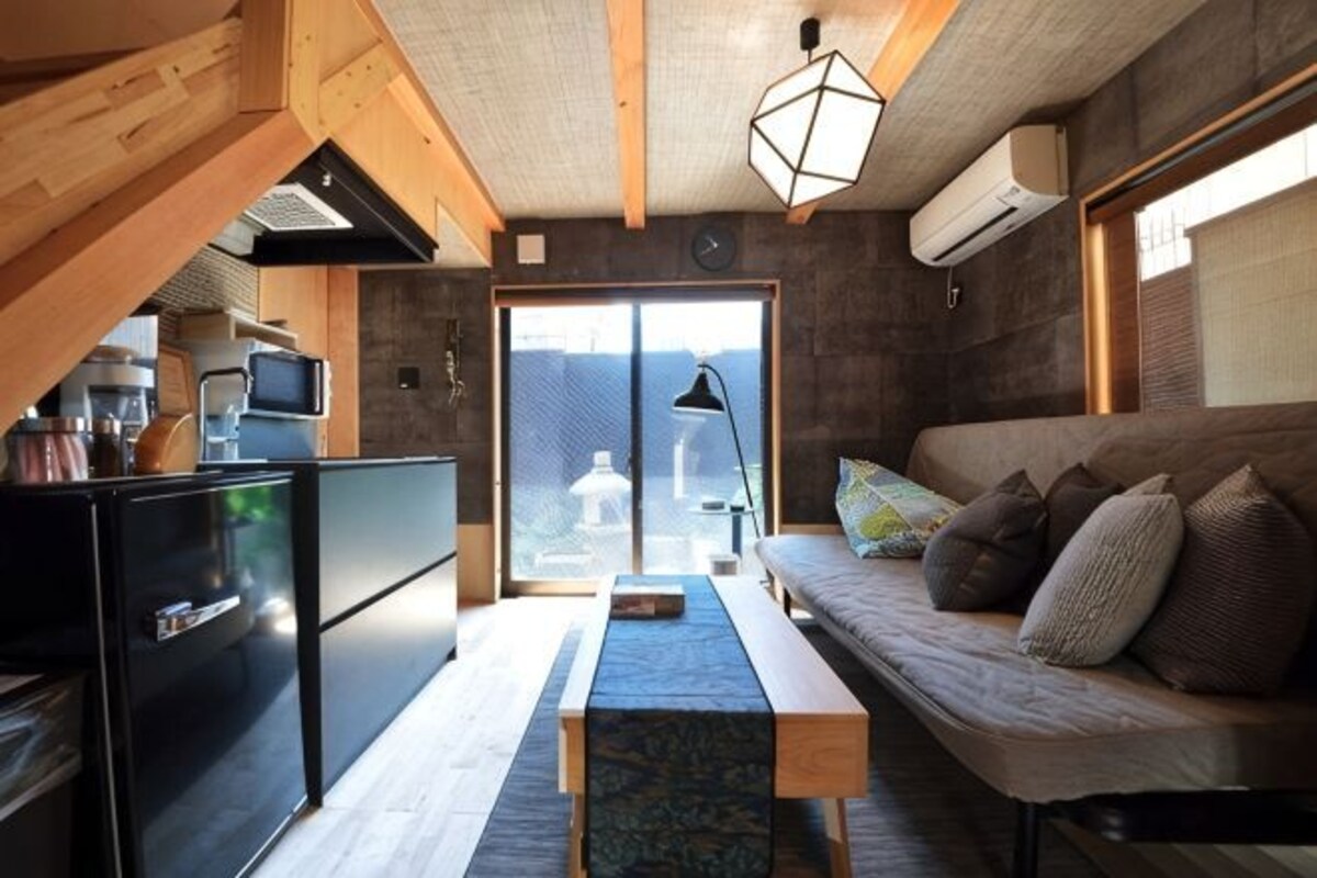 Un espacio habitable compacto con kitchenette, un sofá, una mesa de comedor y un ventanal grande.
