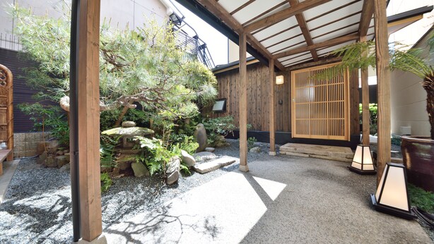 Un jardín japonés tradicional con construcciones de madera, faroles de piedra y diversas plantas.
