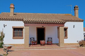 A traditional building with a tiled roof, a central doorway, and two chairs outside.