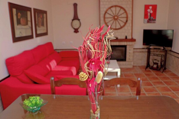 A living room with a red sofa, a fireplace, a television, and a vase with flowers on a table.