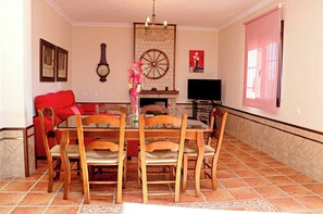 A dining area with a wooden table and chairs, a red sofa, a clock, a TV, and a fireplace.