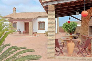 A patio area with a table and chairs, a brick wall, and a building with a tiled roof. - Rustic holiday villa for 5 people (CONIL DE LA FRONTERA)