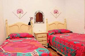 A bedroom with two beds, each with a colorful quilt, a nightstand with a lamp, and a mirror on the wall.
