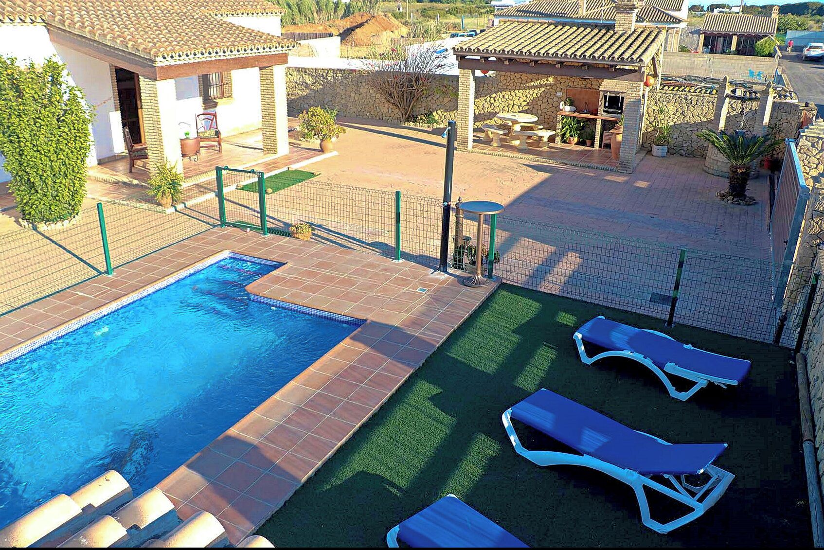 A swimming pool with a tiled deck, lounge chairs, and a stone wall.
