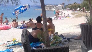 A beach scene with people relaxing on the sand, some under umbrellas, and a few in the water. - Modern apartment near Split and Trogir (Kaštel Gomilica)
