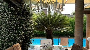 Ein Esstisch im Freien mit Blick auf einen Pool, umgeben von Stühlen und einem dekorativen Kronleuchter.
