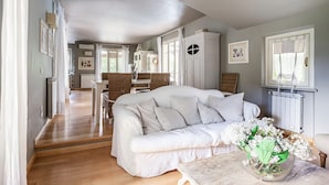 Ein geräumiges Wohnzimmer mit einem weißen Sofa, einem Essbereich mit Korbstühlen und einer Küche im Hintergrund.