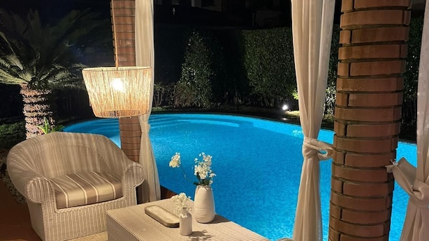 Ein Sitzbereich am Pool mit Korbmöbeln und einem Tisch, mit Blick auf ein Nachtschwimmbad.