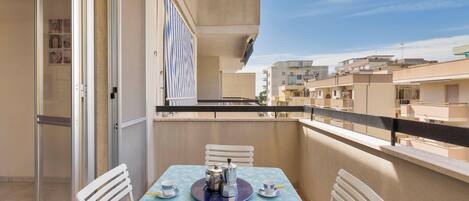 Varanda com mesa posta para dois, porta de correr e vista para edifícios vizinhos.