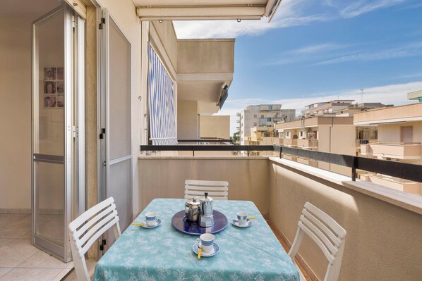 A balcony with a table set for two, a sliding door, and a view of neighboring buildings.
