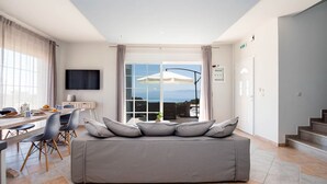 Een moderne woonkamer met een bank, eethoek en een groot raam met uitzicht op de zee.