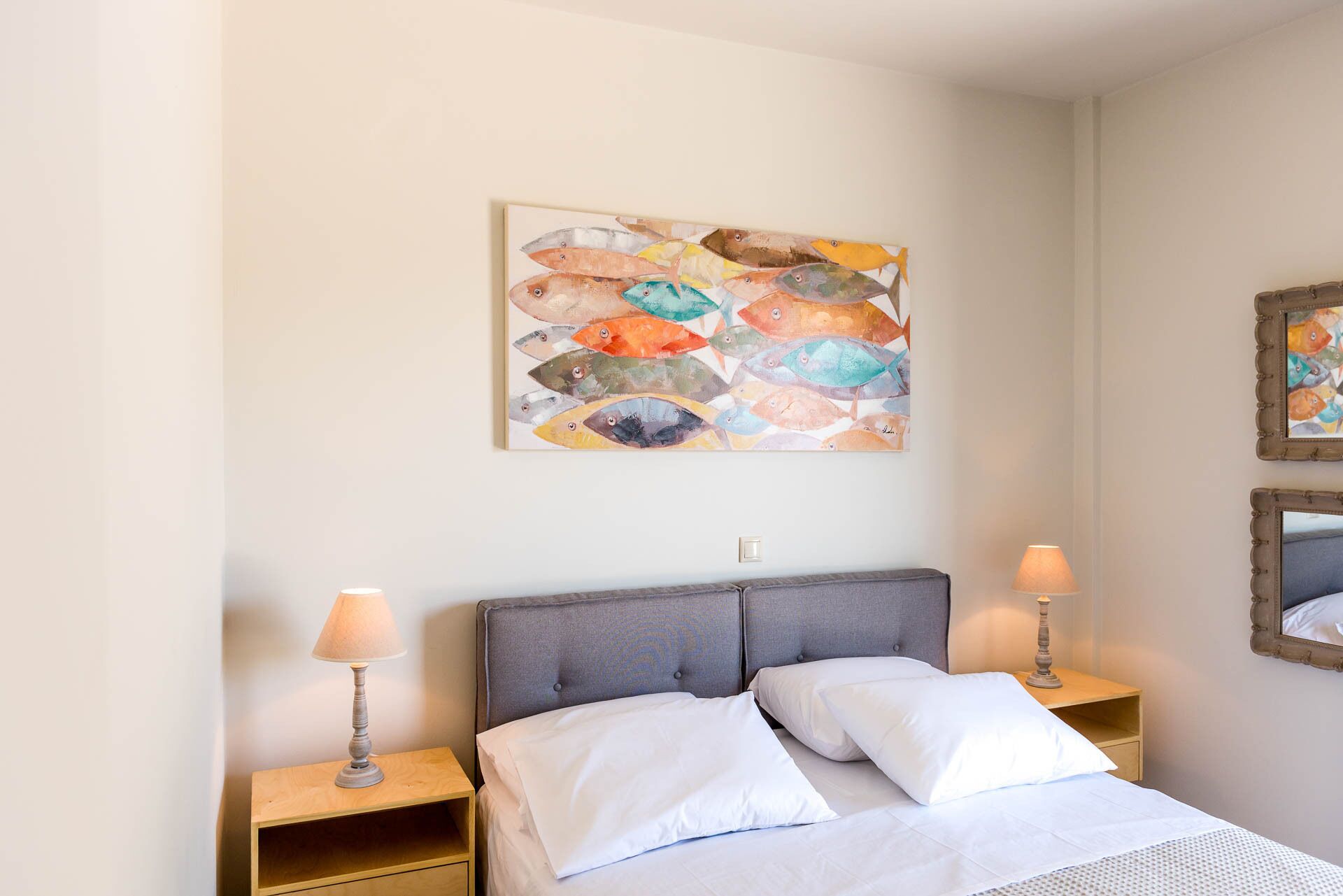 A bedroom with a bed, two nightstands, two lamps, and a colorful fish painting on the wall.