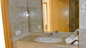 Ein Badezimmer mit Marmorwand, einem Holzlagerraum, einem Waschbecken und einem Spiegel.