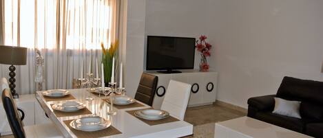 A modern living room with a dining area, a flat-screen TV, and a sofa.