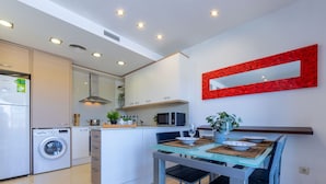 A modern kitchen with built-in appliances, a dining area with a glass table, and a red-framed mirror on the wall.