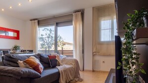 A modern living room with a grey sofa, a dining table with chairs, and a large window with curtains.