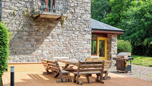 A stone building with a wooden deck, outdoor seating, and a barbecue grill. - 18th Century Coachhouse in a Courtyard Setting (Inistioge)