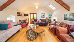 A spacious loft with high ceilings, exposed wooden beams, and a wooden floor. There are multiple seating areas with sofas and a dining table. - 18th Century Coachhouse in a Courtyard Setting (Inistioge)