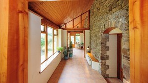 A wooden hallway with a stone wall, large windows, and potted plants. - 18th Century Coachhouse in a Courtyard Setting (Inistioge)