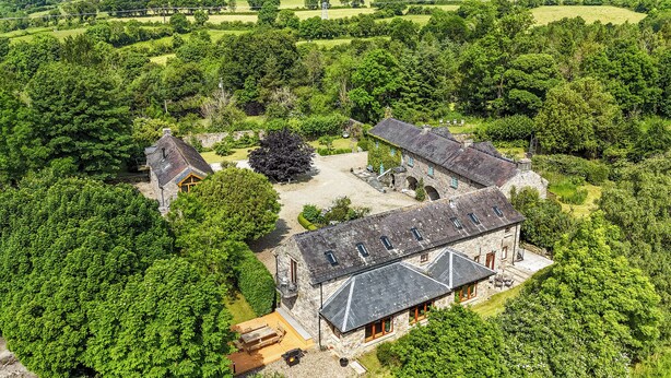 A stone building with a large patio area, surrounded by dense greenery. - 18th Century Coachhouse in a Courtyard Setting (Inistioge)