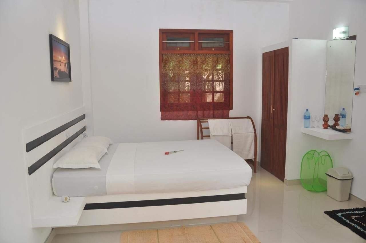 A bedroom with a bed, a window with a curtain, a wardrobe, a mirror, and a shelf with toiletries.