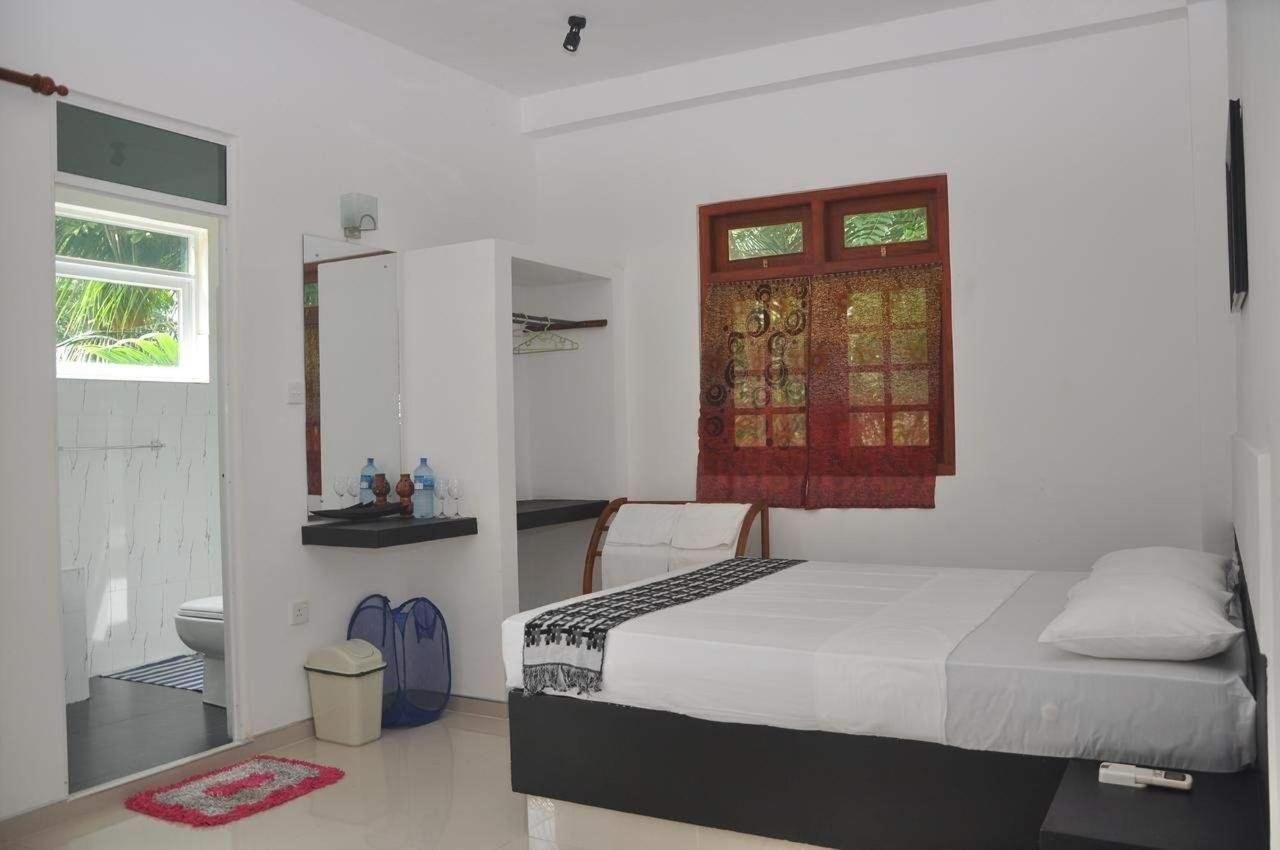 A bedroom with a bed, a window with decorative curtains, a bedside table, and a mirror.