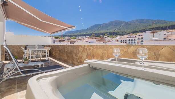 Una terraza en la azotea con jacuzzi, mobiliario exterior y vistas a un pueblo y montañas.
