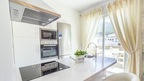 Una cocina moderna con electrodomésticos integrados, una encimera blanca y vistas al exterior a través de amplias ventanas.