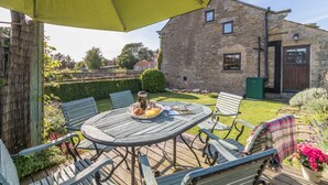 A wooden deck with a table and chairs, a yellow umbrella, and a stone building in the background. - The Cottage Gillamoor York, with wood burner, wifi and good local pub (Gillamoor)