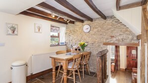 A rustic dining area with a stone wall, wooden ceiling beams, a clock, and a table with chairs. - The Cottage Gillamoor York, with wood burner, wifi and good local pub (Gillamoor)