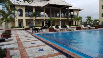 A hotel with a swimming pool, outdoor seating, and palm trees.