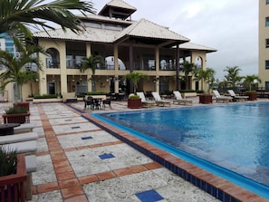A hotel with a swimming pool, outdoor seating, and palm trees.