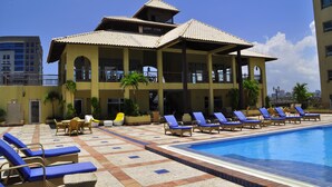 Hotel com piscina, cadeiras de sol e área coberta com mesas e cadeiras.