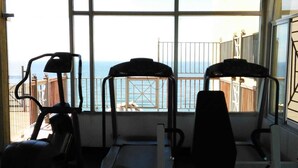 Uma academia com equipamentos de ginástica e vista para o oceano através de grandes janelas.