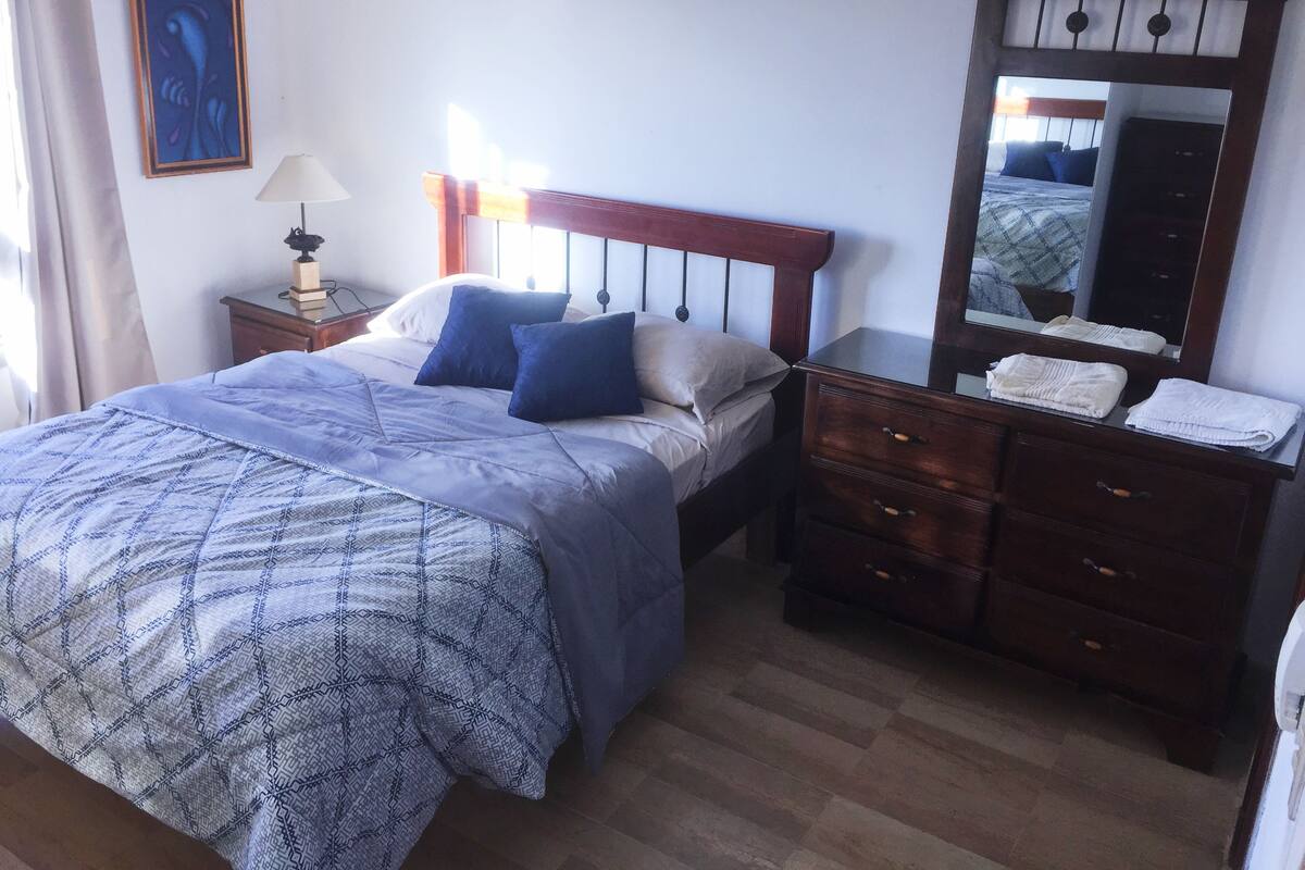A neatly arranged bedroom with a bed, bedside table, dresser, and a mirror.
