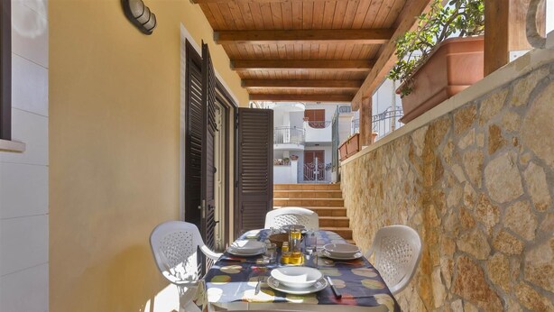 A covered outdoor dining area with a table set for four, surrounded by stone walls and wooden beams. - Girasole Trilo 2 by BarbarHouse (Castrignano del Capo)