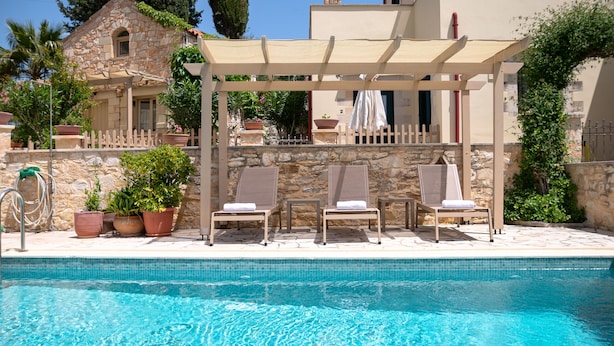 Uma área à beira da piscina com espreguiçadeiras, um pergolado e plantas em vasos.