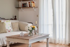 Une pièce comprenant un lit, une table en bois ornée d’un vase de fleurs, une bougie et une bibliothèque.