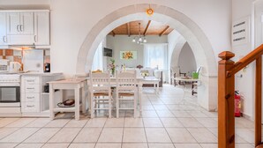 A kitchen with white cabinets, a dining area with a table and chairs, and a wooden staircase. - Helianthos 1 ,Douliana, Near Vamos & Almirida (Chania)