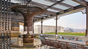 Un bar moderno con una zona de estar circular central, una estantería para vinos y vistas a edificios y montañas distantes.