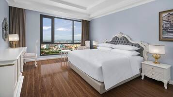 Un dormitorio con una cama grande, una mesita de noche, una silla y vistas a un paisaje urbano a través de un ventanal.