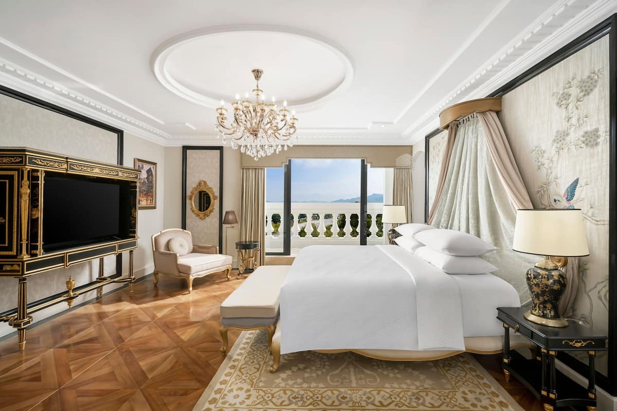 Une chambre à coucher luxueuse, dotée d’un grand lit, d’une télévision, d’un lustre et offrant une vue sur la mer.